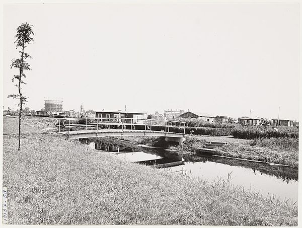 Hier ziet u het bruggetje naar het eiland in 1954. In de verte links de gesloopte gasfabriek en het de nog overeind staande watertoren.